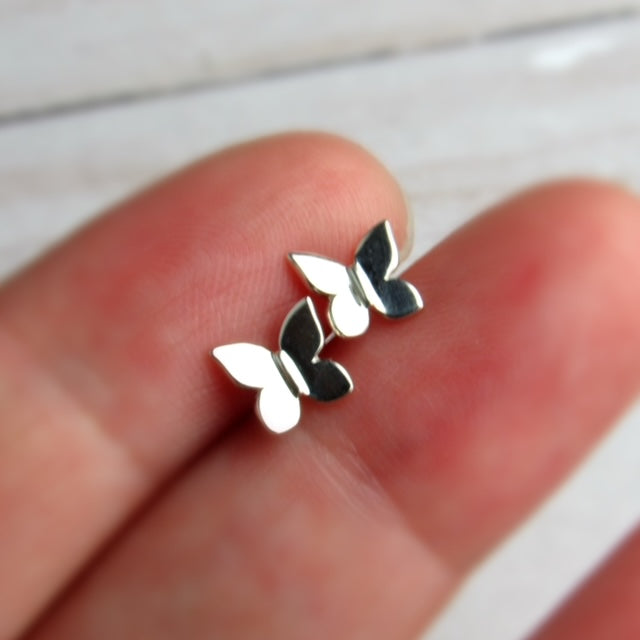 Silver butterfly earrings held between two fingers