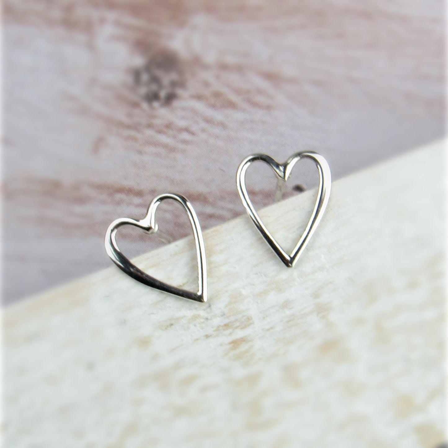 Silver heart-shaped earrings on a light wooden surface