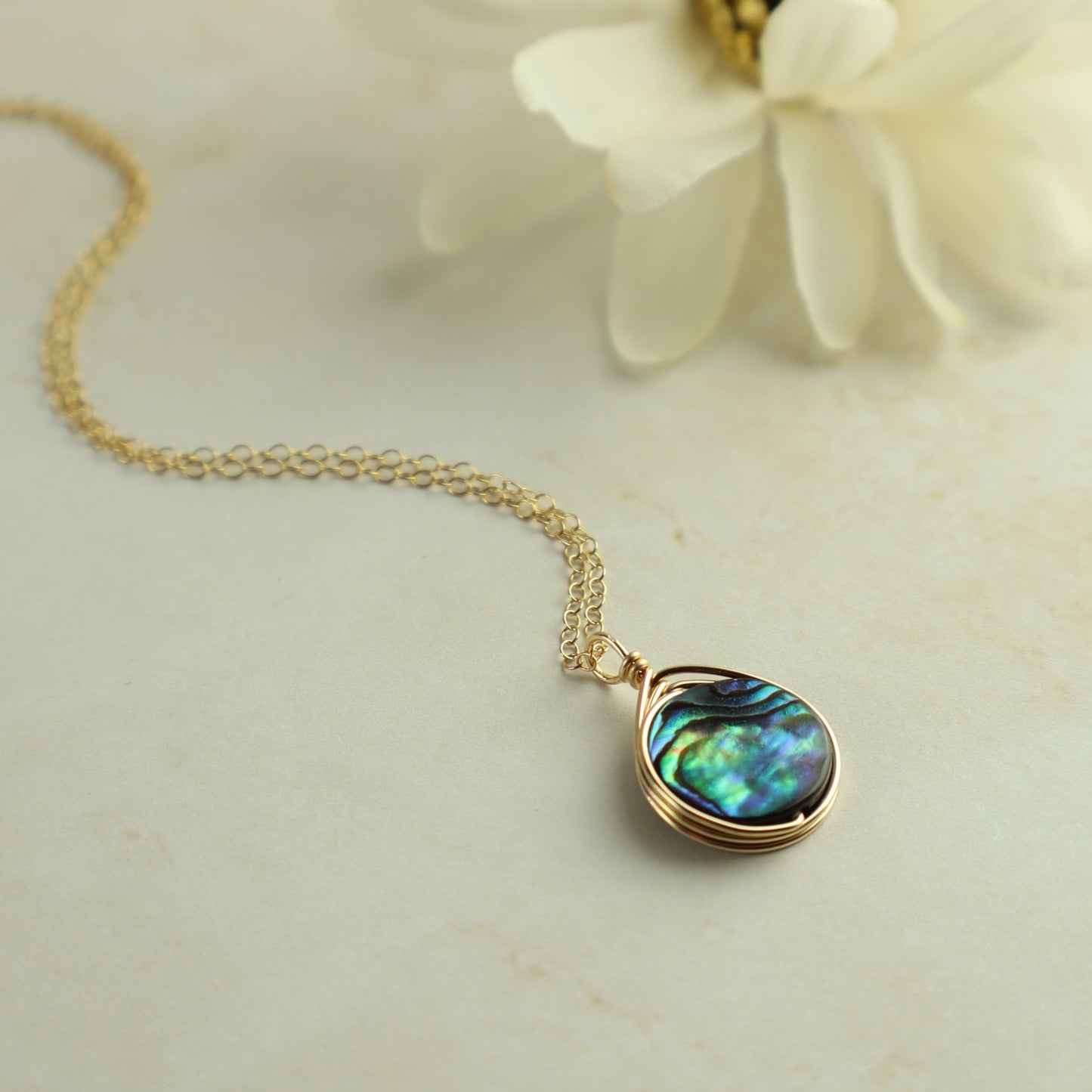 Gold necklace with a teardrop-shaped abalone shell pendant on a light background