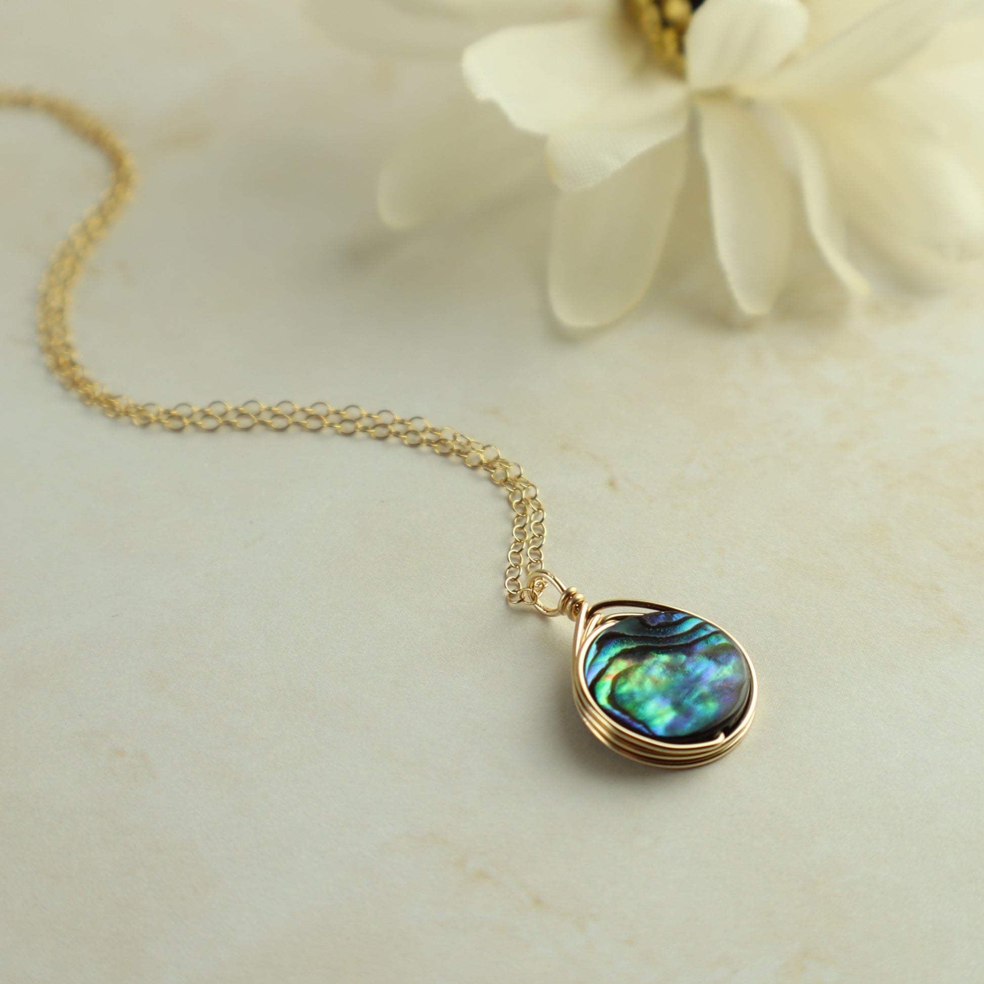Gold necklace with a teardrop-shaped abalone shell pendant on a light background