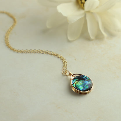 Gold necklace with a teardrop-shaped abalone shell pendant on a light background
