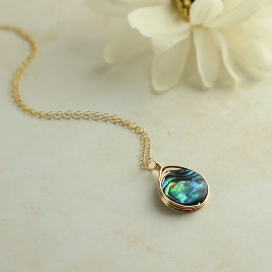 Gold necklace with a teardrop-shaped abalone shell pendant on a light background