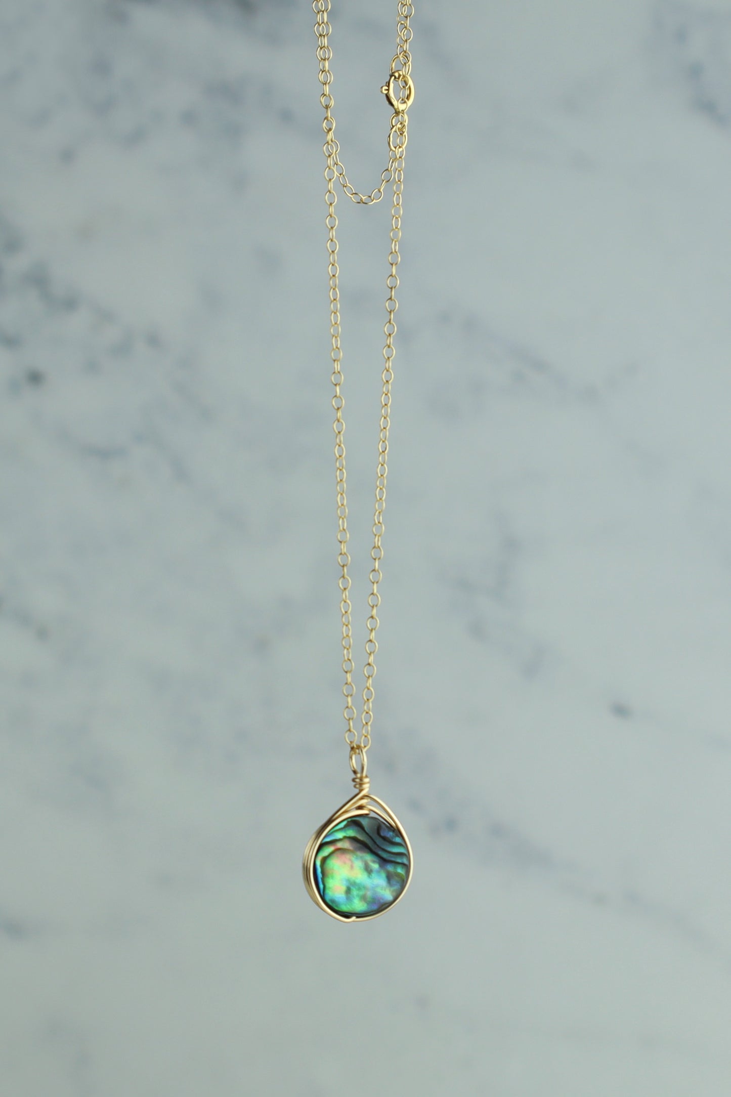 Gold necklace with a teardrop-shaped green pendant on a marble background