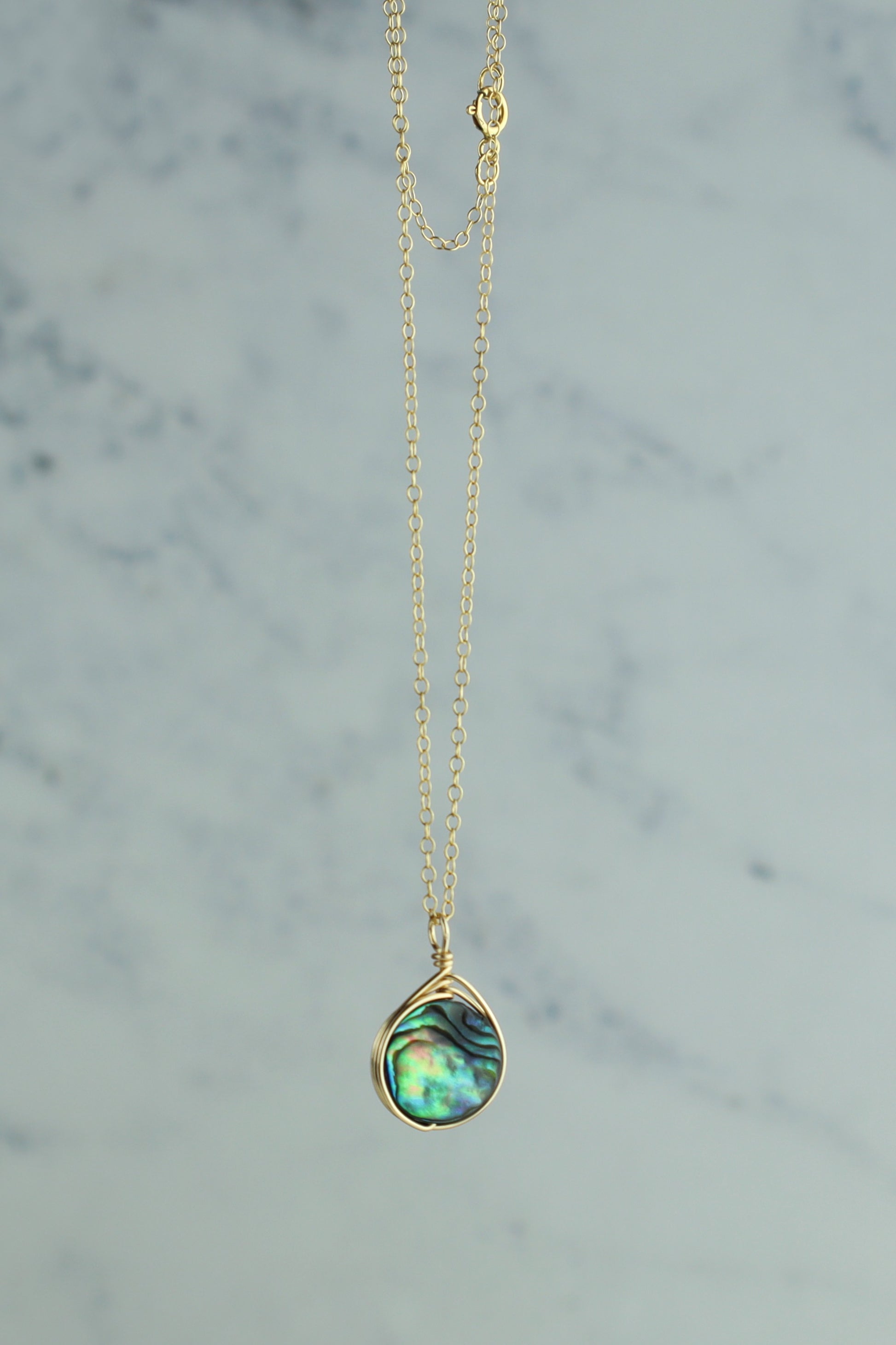 Gold necklace with a teardrop-shaped green pendant on a marble background