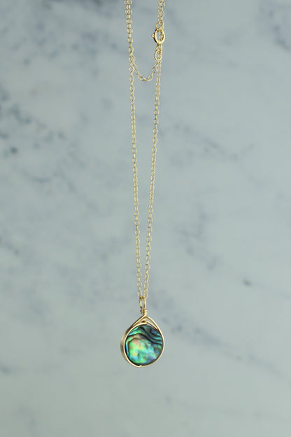 Gold necklace with a teardrop-shaped green pendant on a marble background