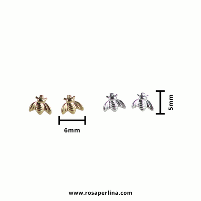 Two pairs of small bee-shaped stud earrings shown on a plain white background, with size markers indicating 6mm width for the left pair and 5mm width for the right pair. One pair is gold-toned and the other is silver-toned.