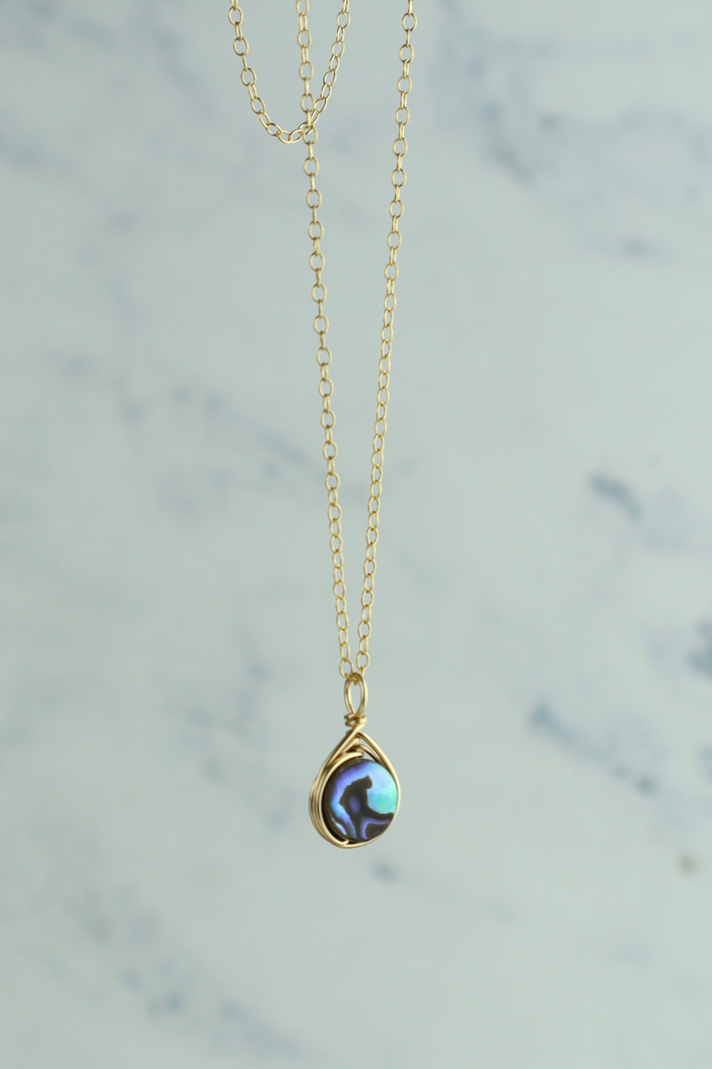 Gold necklace with an abalone pendant on a light gray background