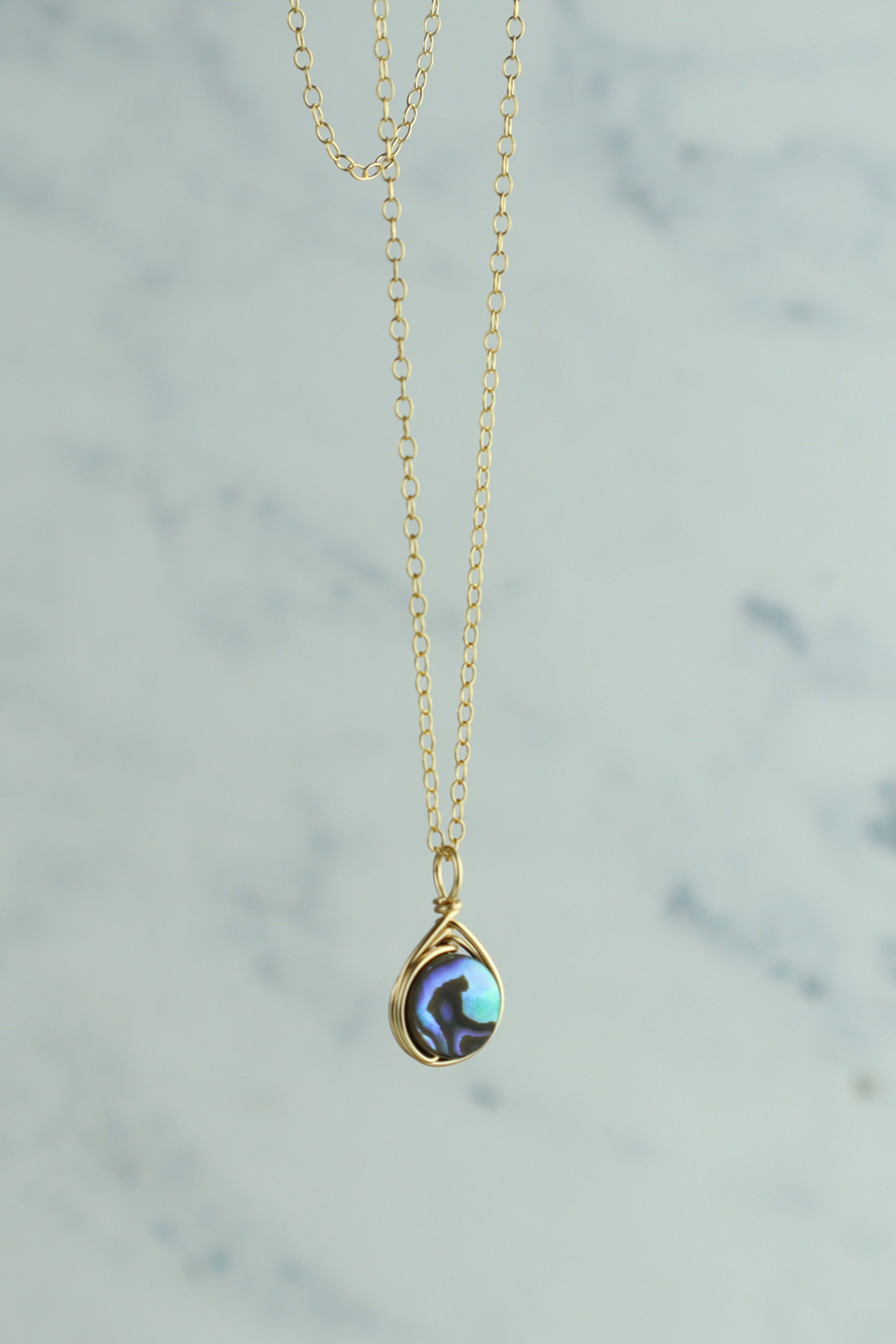 Gold necklace with an abalone pendant on a light gray background