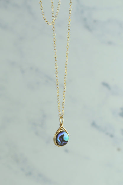 Gold necklace with an abalone pendant on a light gray background