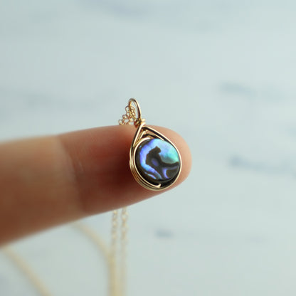 Gold abalone pendant necklace on a fingertip with a blurred background