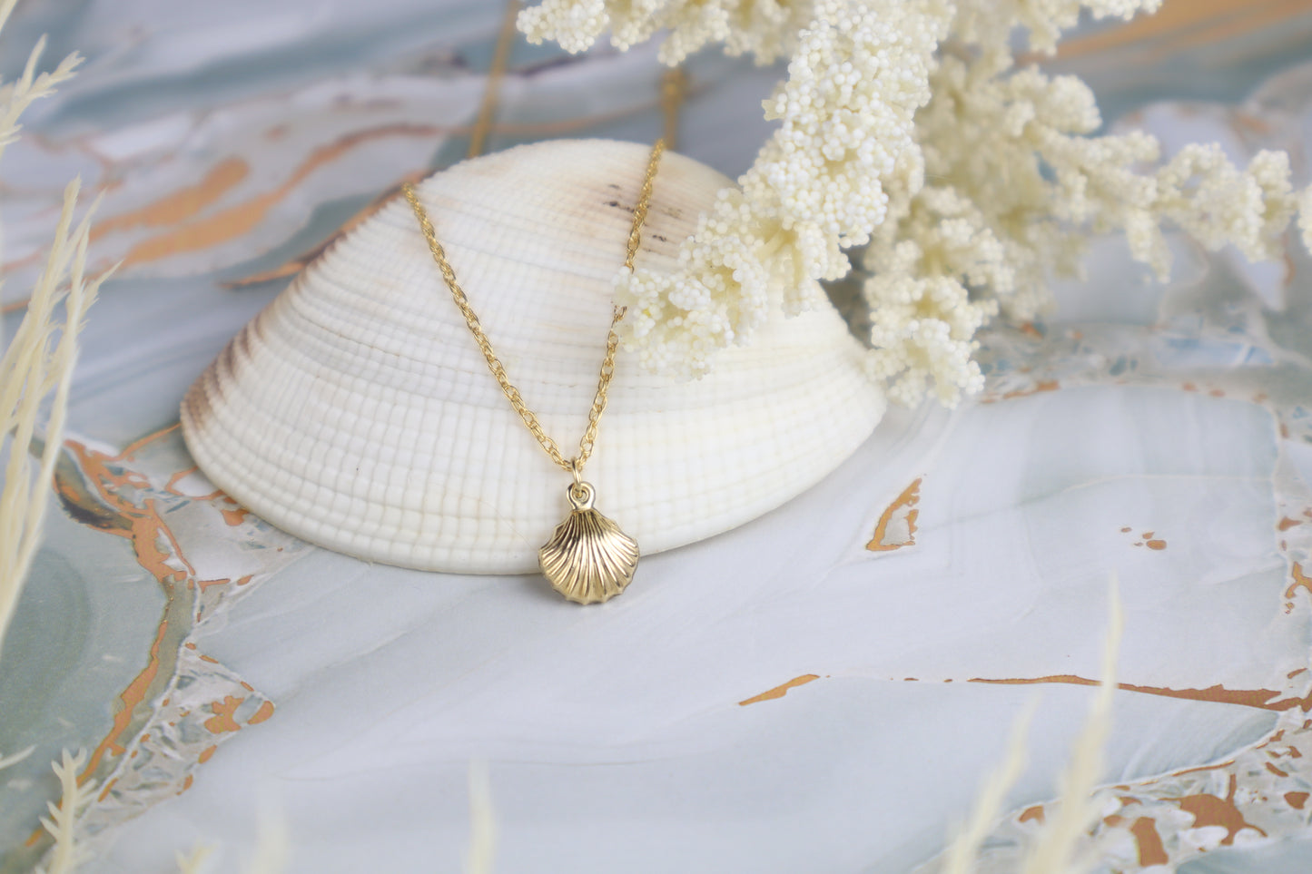 Gold necklace with a shell pendant on a decorative surface with a shell and flowers.