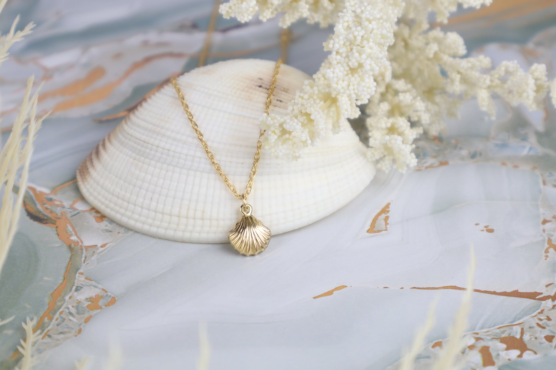 Gold necklace with a shell pendant on a decorative surface with a shell and flowers.