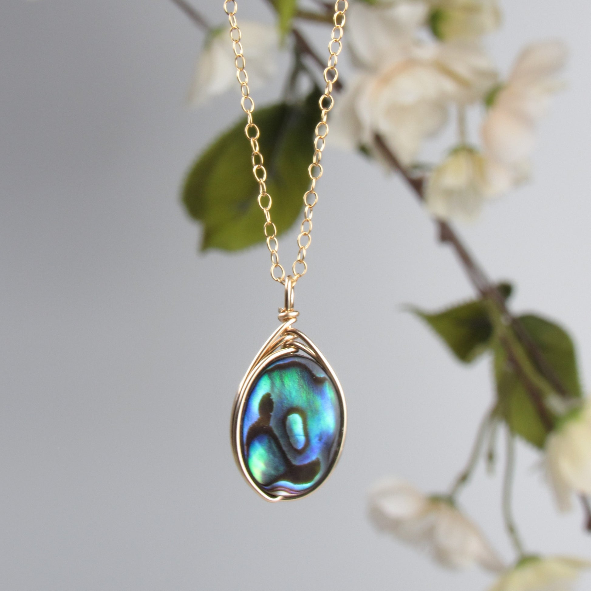 Necklace with a paua shell pendant against a soft floral background