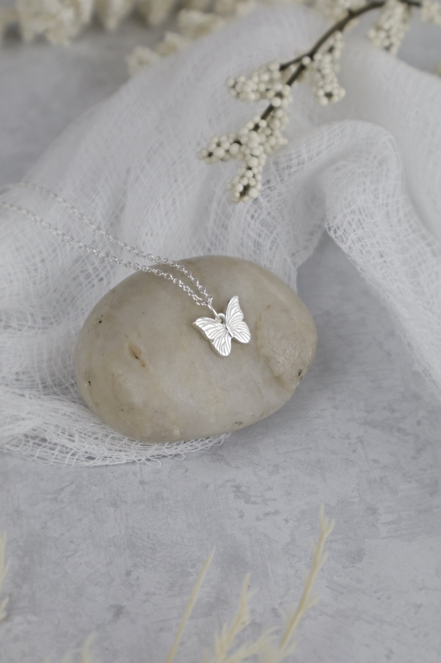 Silver butterfly necklace on a stone with delicate flowers in the background