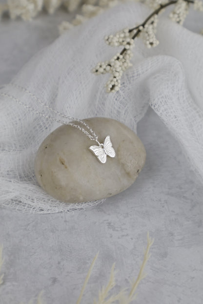 Silver butterfly necklace on a stone with delicate flowers in the background