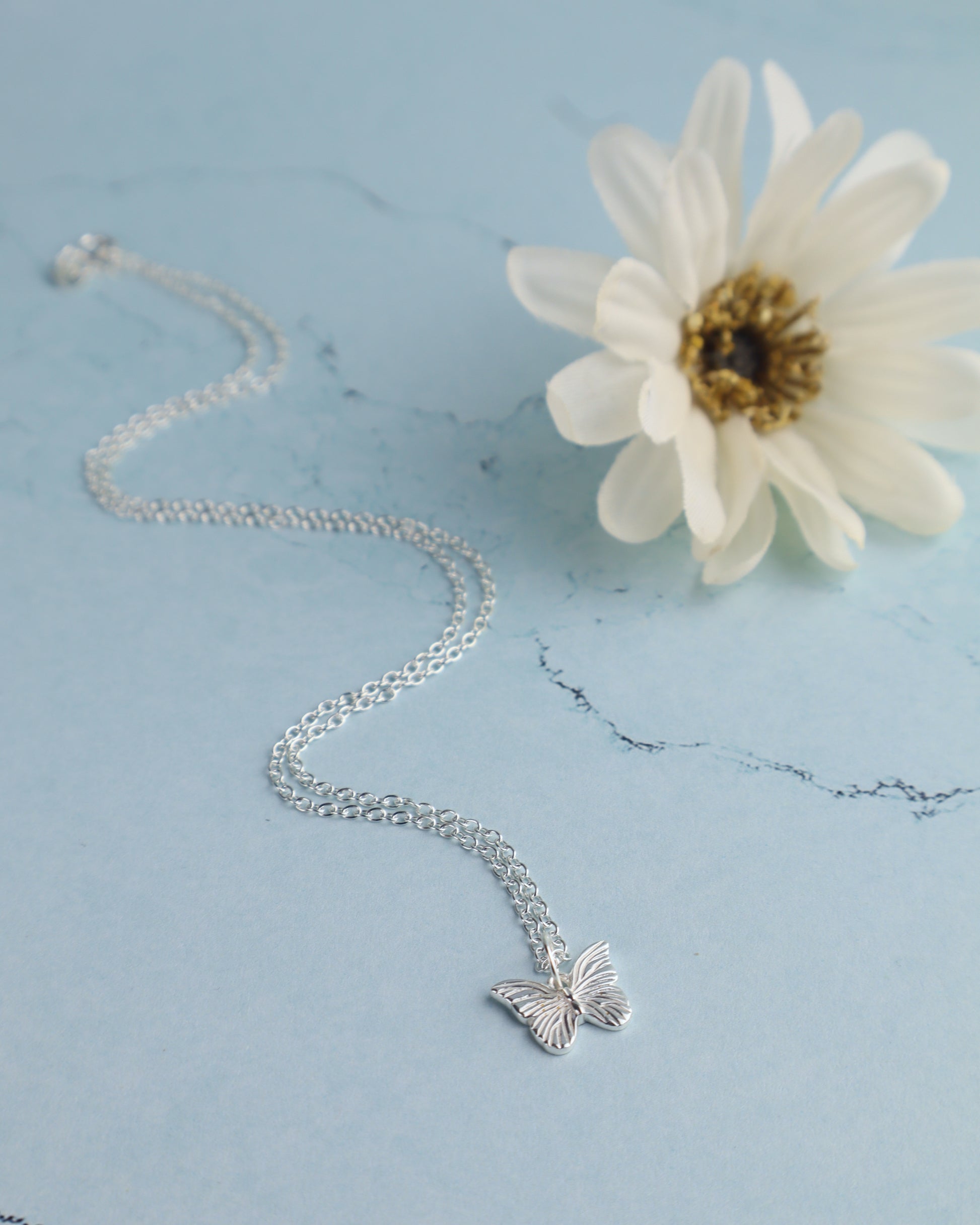 sterling silver butterfly pendant necklace resting on a blue marble surface with a  flower