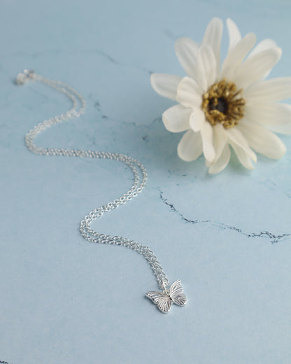 sterling silver butterfly pendant necklace resting on a blue marble surface with a  flower