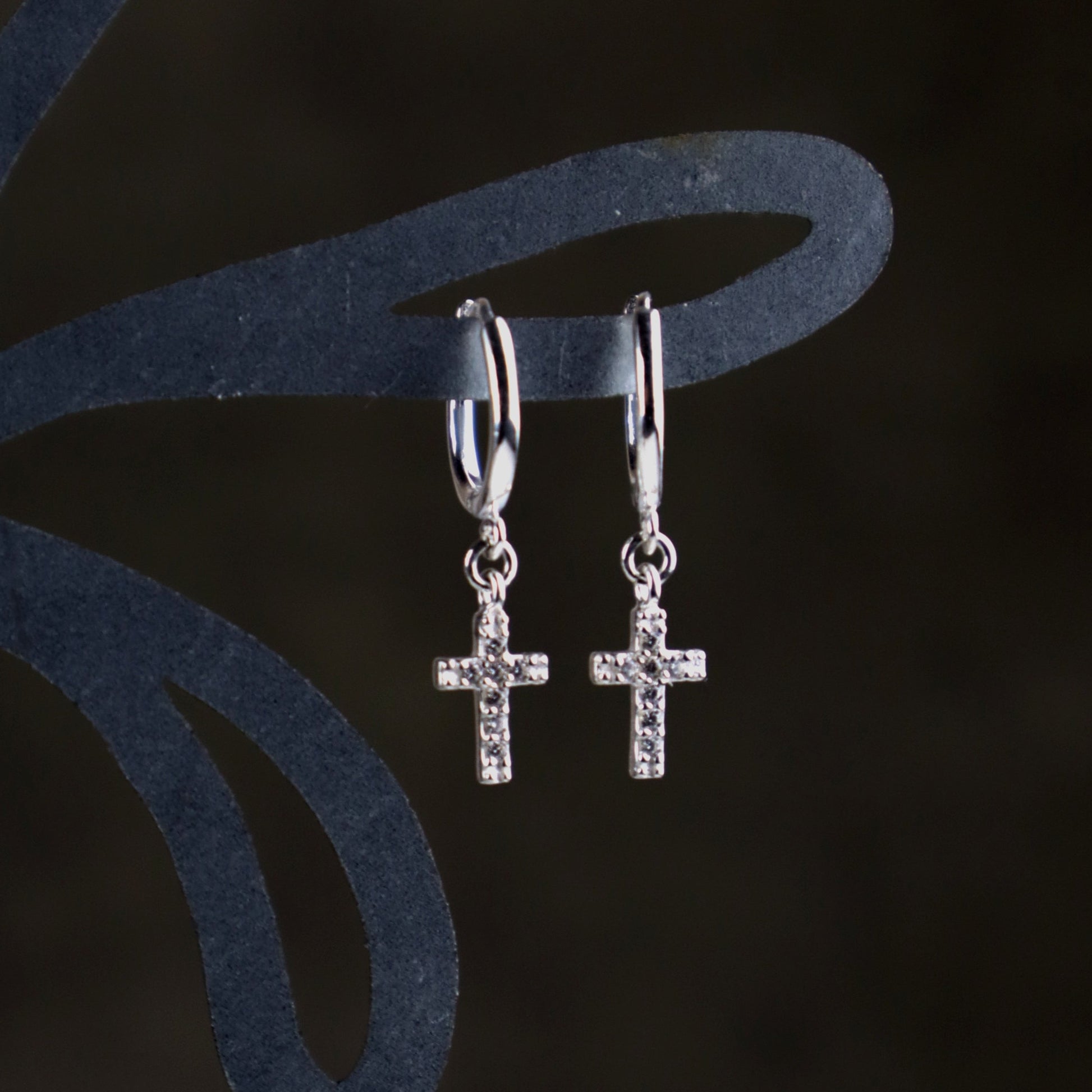 Sterling Silver cross huggie earrings on a dark background