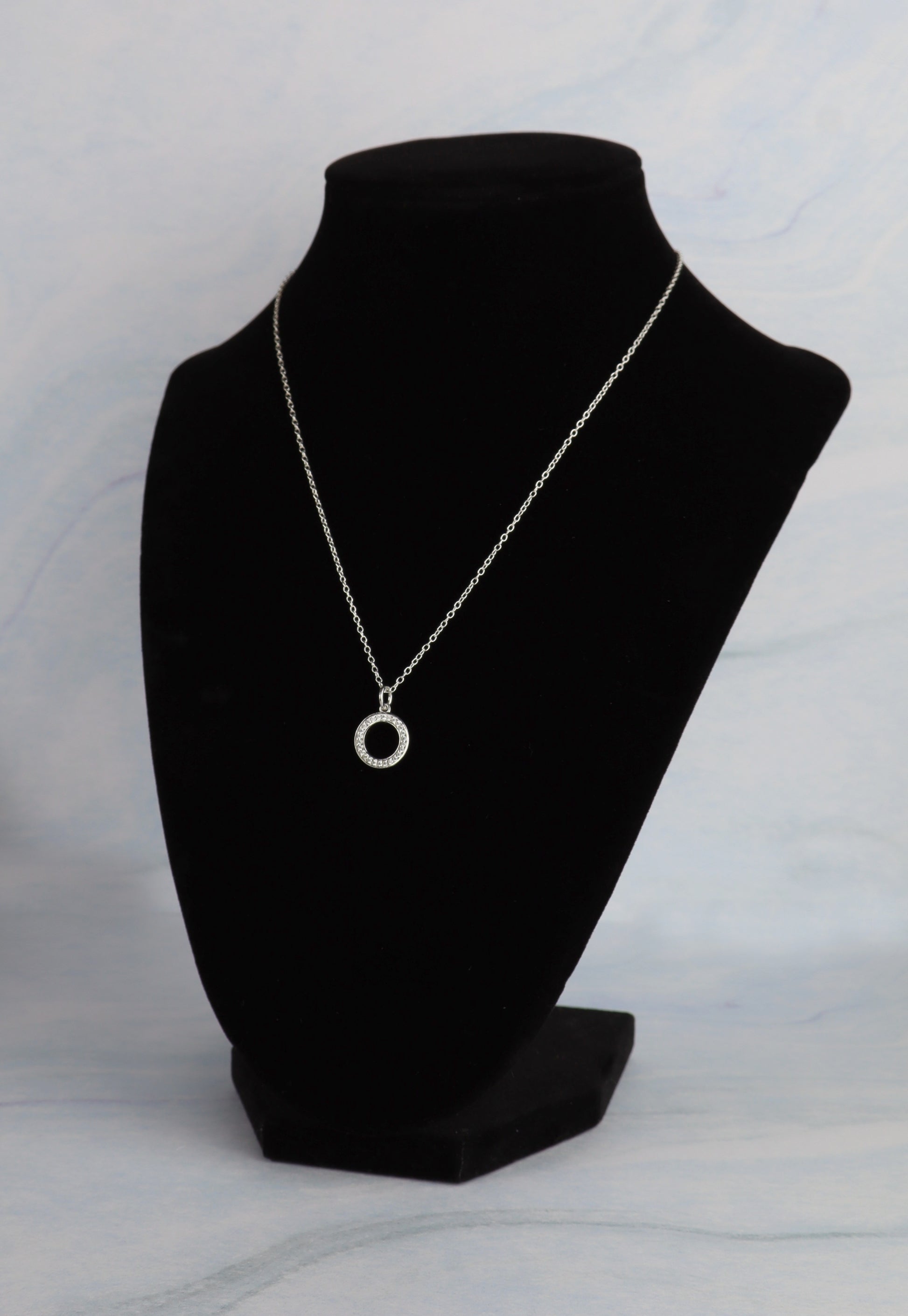 Necklace with a circular pendant on a black mannequin bust against a light gray background