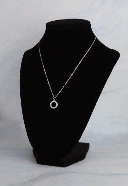 Necklace with a circular pendant on a black mannequin bust against a light gray background