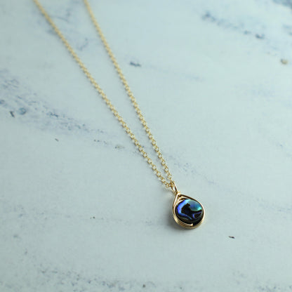 Necklace with a round abalone pendant on a light gray background