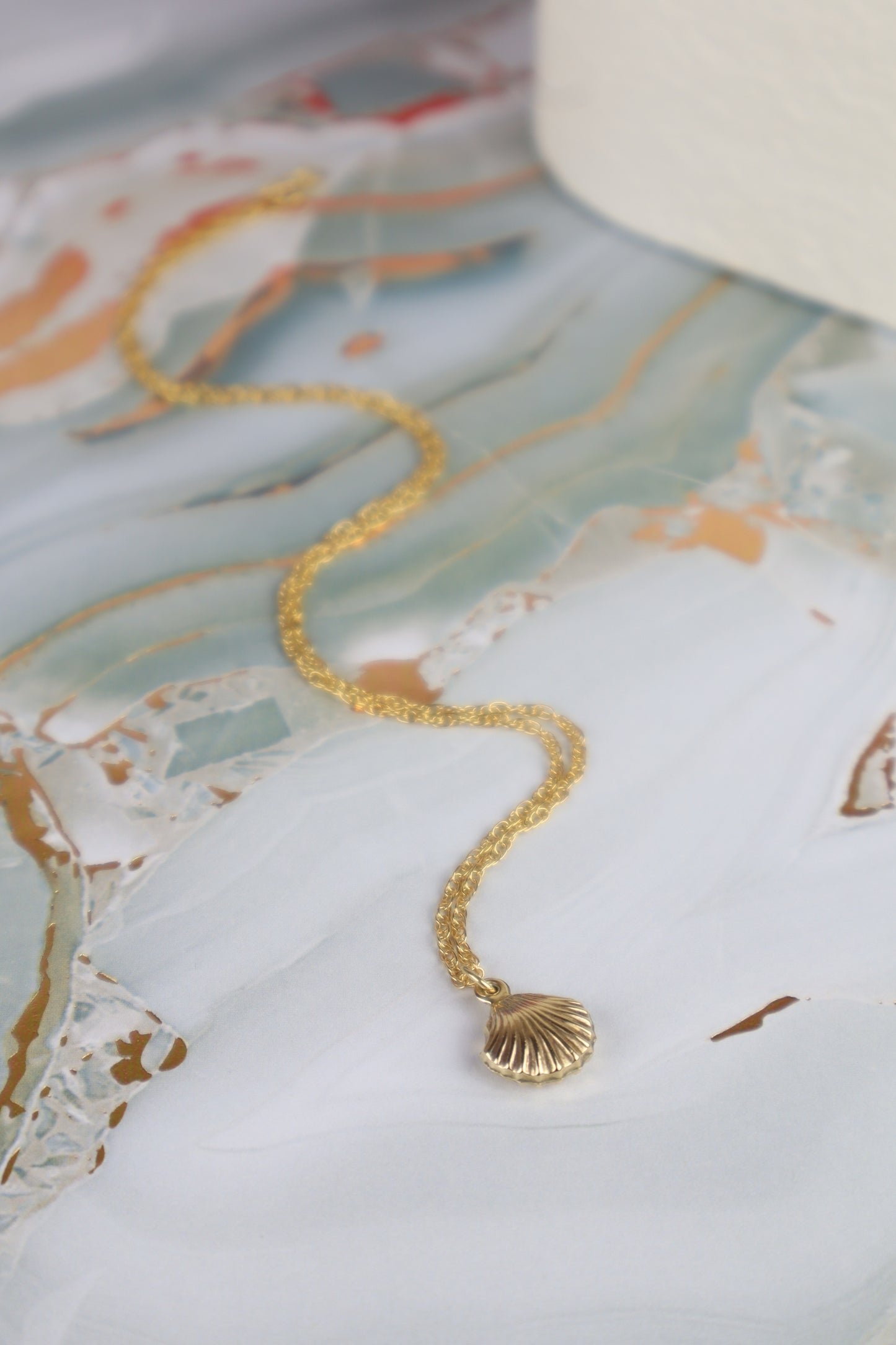 Gold necklace with a shell pendant on a decorative surface