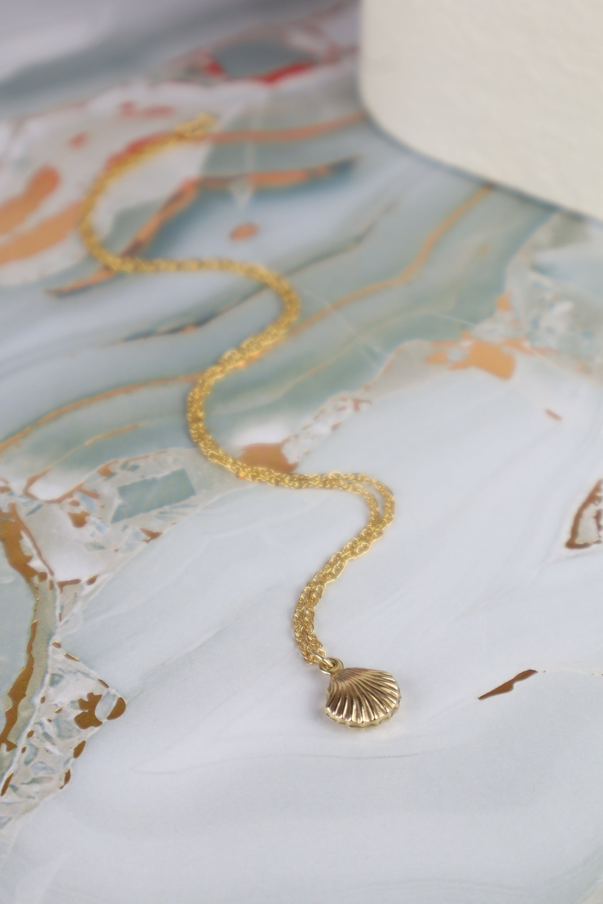 Gold necklace with a shell pendant on a decorative surface