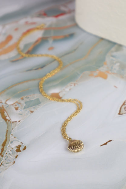 Gold necklace with a shell pendant on a decorative surface