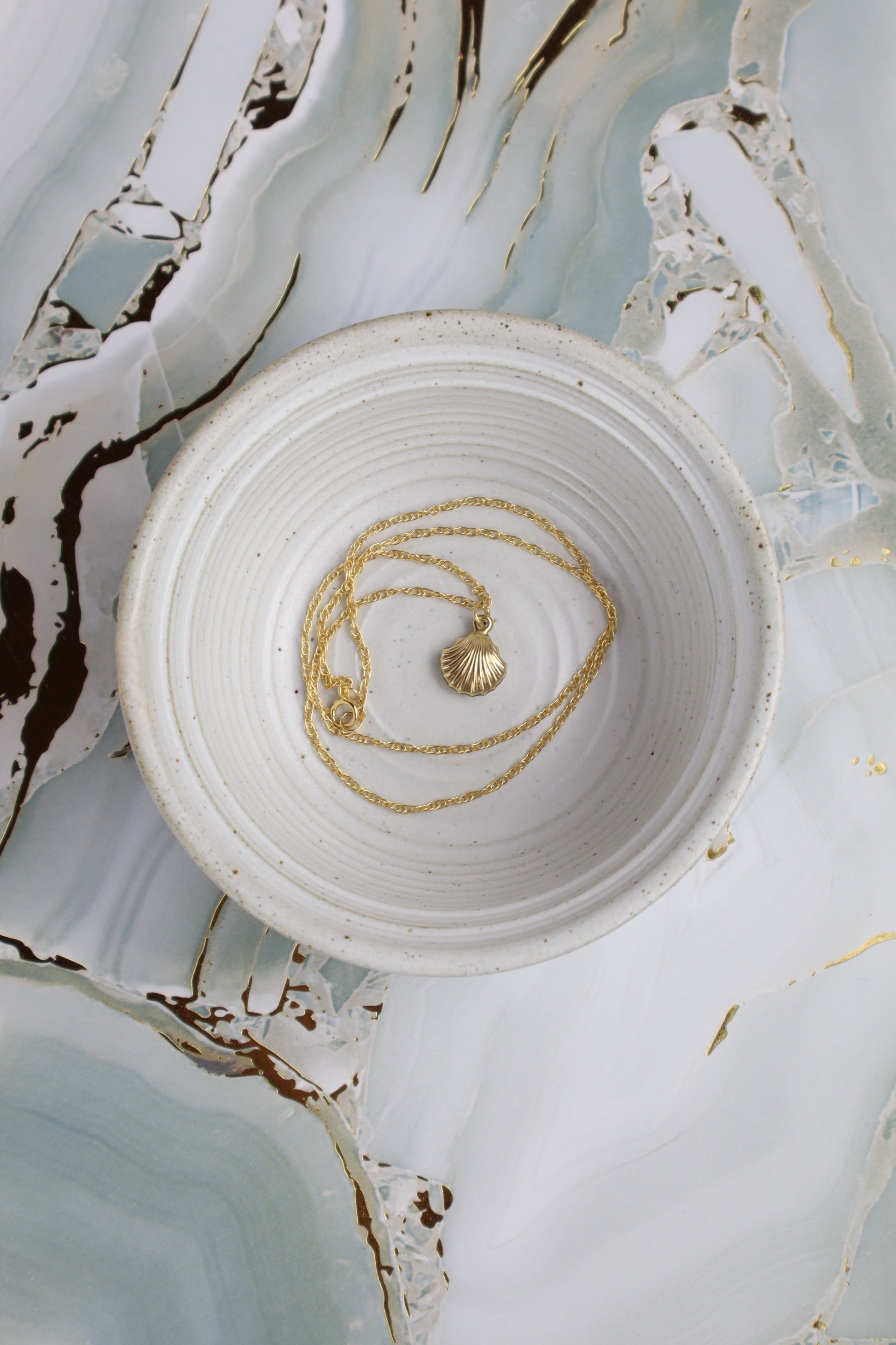 Gold necklace on a white ceramic dish with a marble-like background