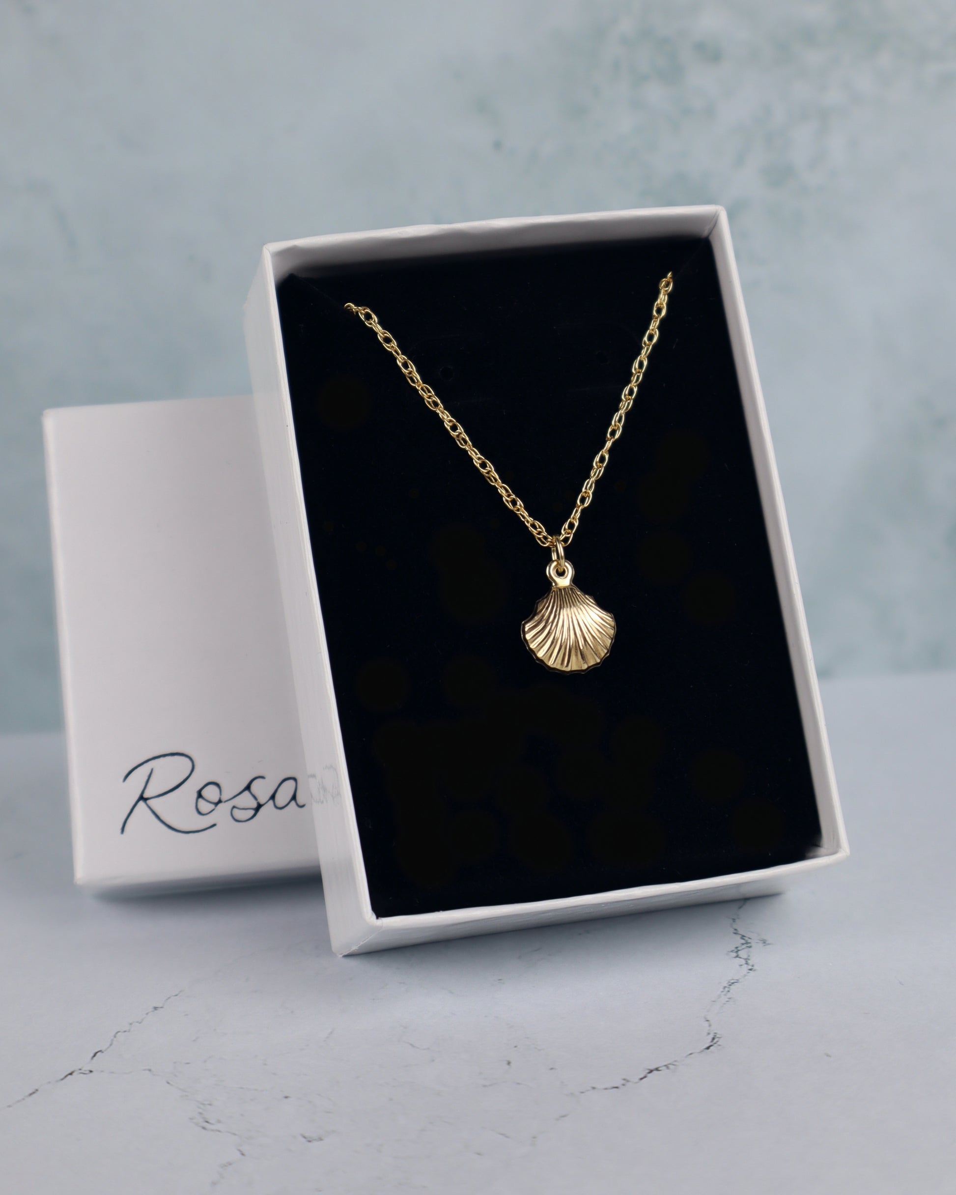 Gold necklace with a shell pendant in a white box labeled 'Rosa'.