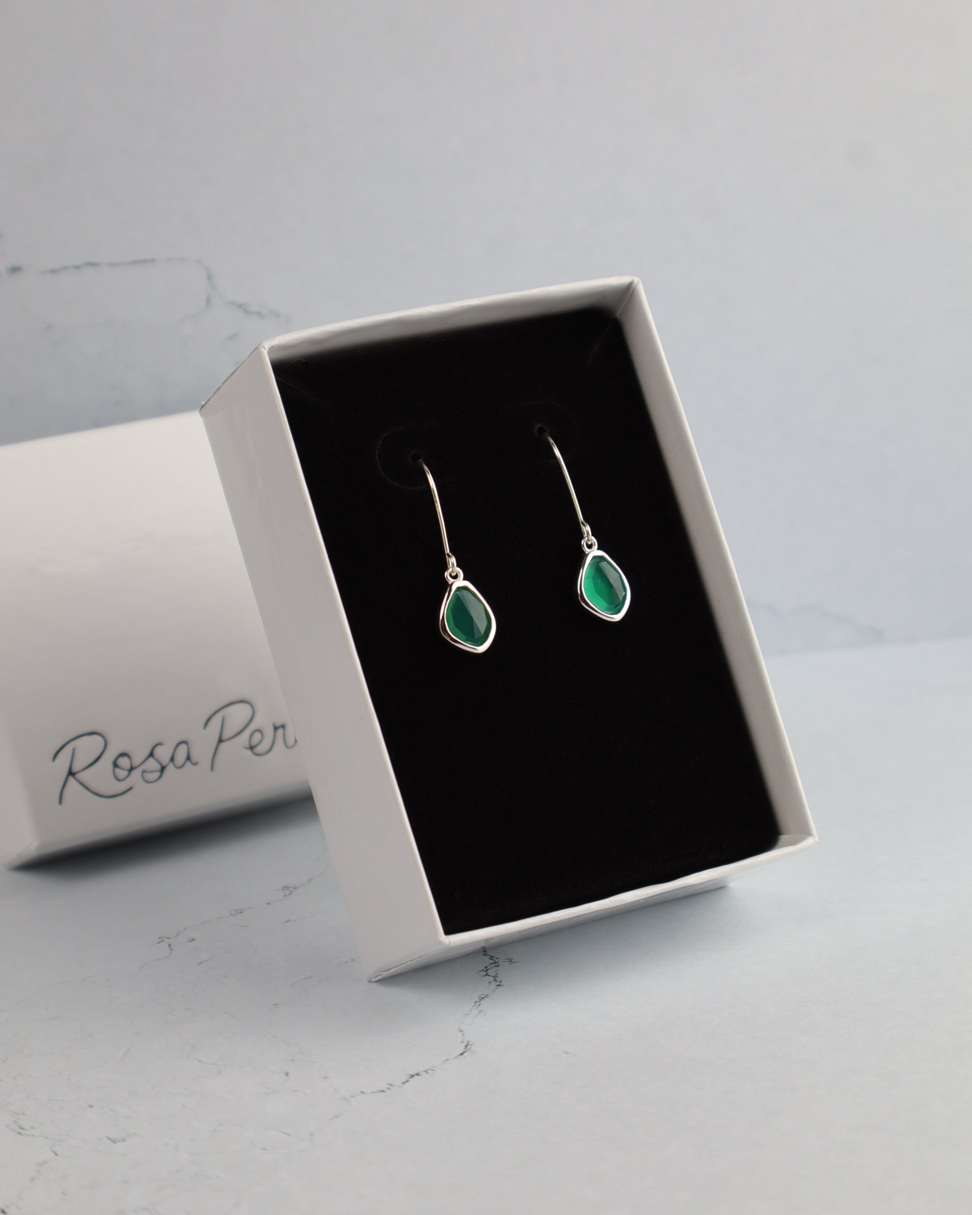 Green teardrop earrings in a 'Rosa Per' jewelry box on a light gray background