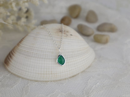 Green teardrop pendant on a silver chain with a shell and stones in the background