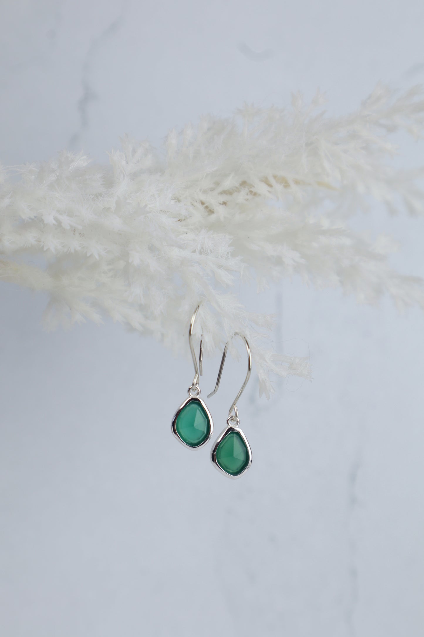 Teardrop-shaped green earrings on a light background