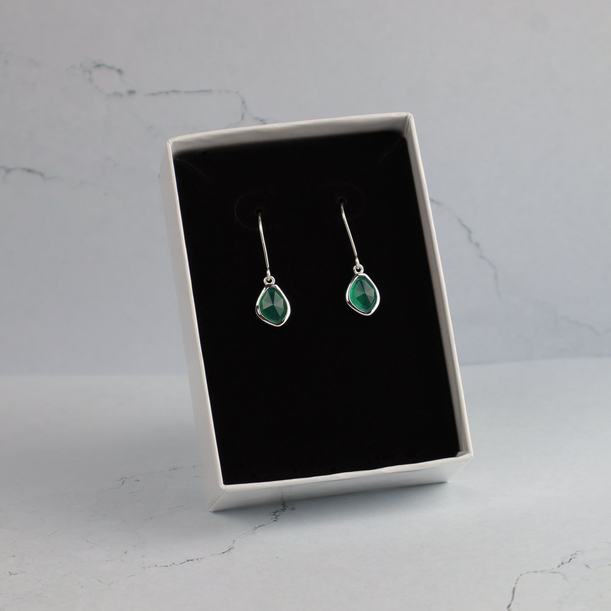 Pair of emerald green teardrop earrings in a black jewelry box on a marble surface