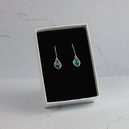 Pair of emerald green teardrop earrings in a black jewelry box on a marble surface