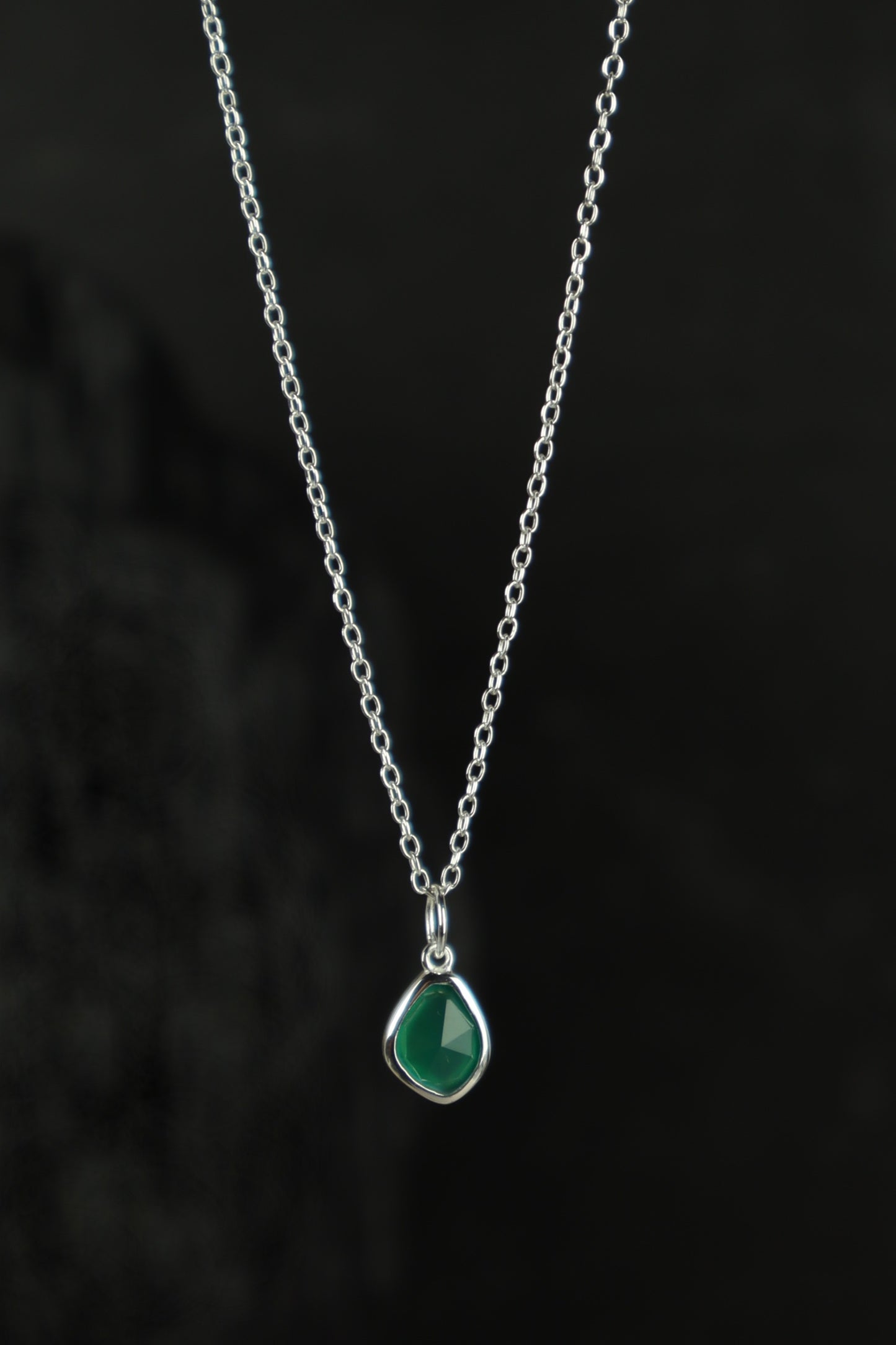 Necklace with a green teardrop pendant on a dark background