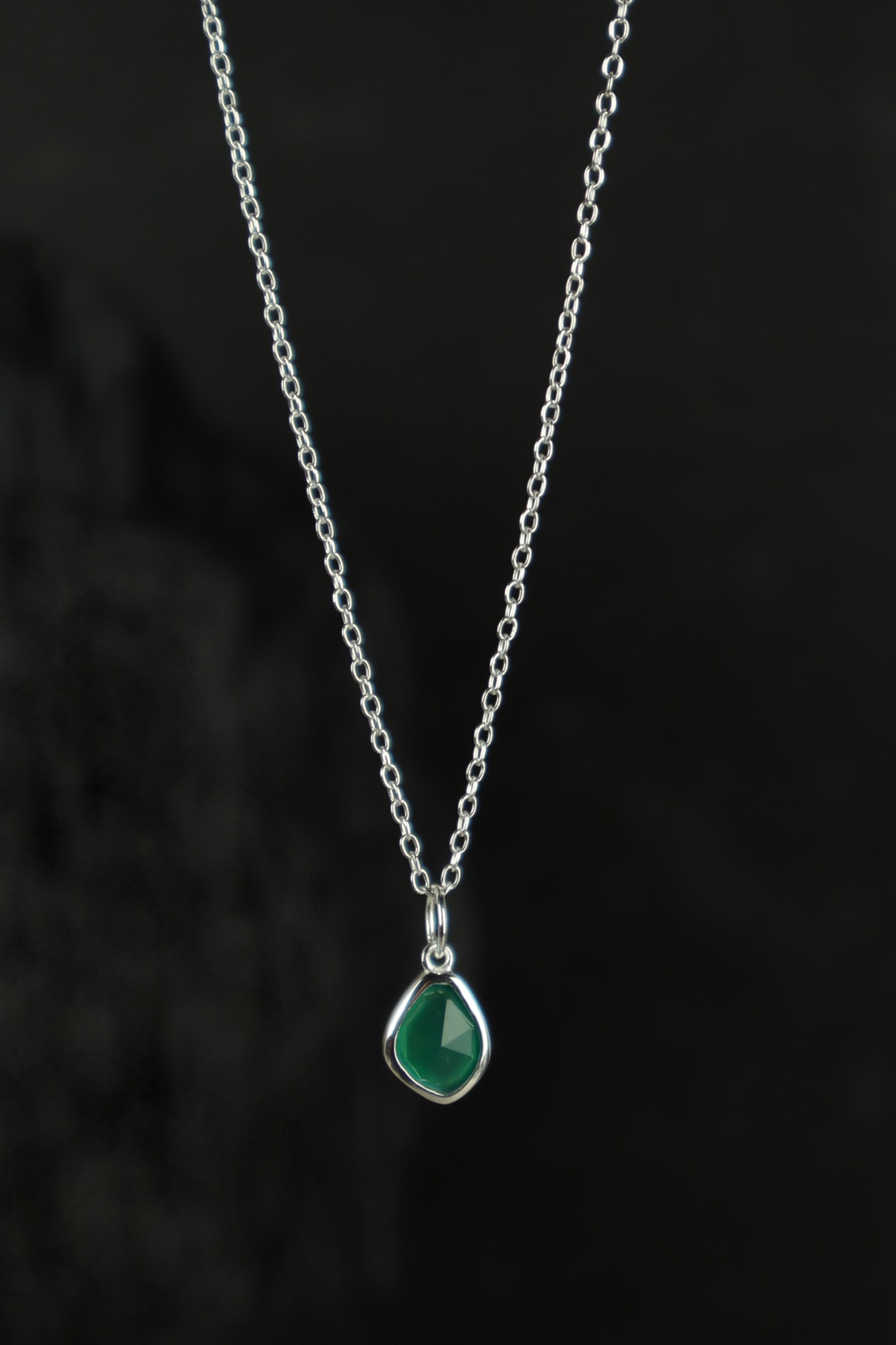 Necklace with a green teardrop pendant on a dark background