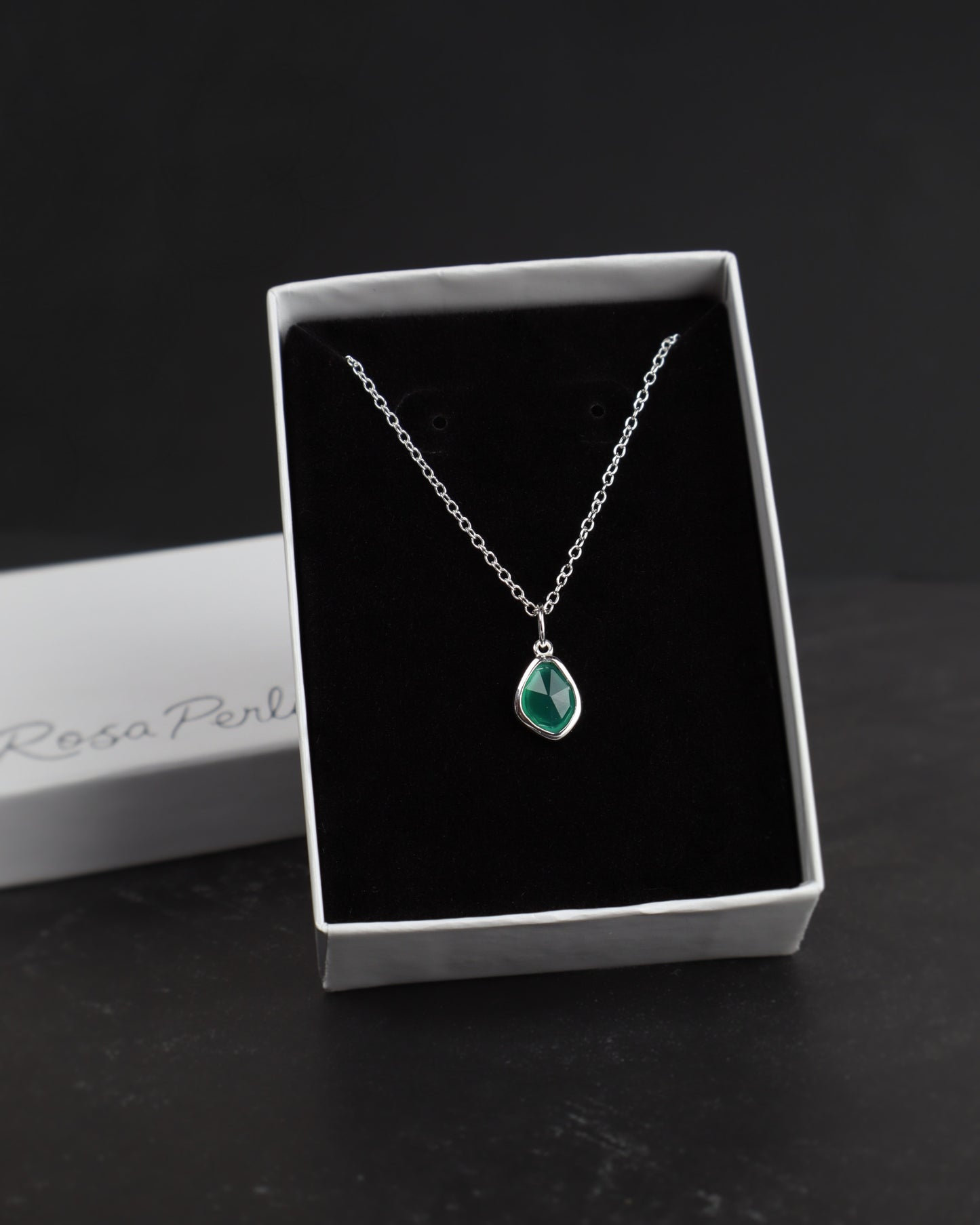 Silver necklace with a green pendant in a white box on a dark surface