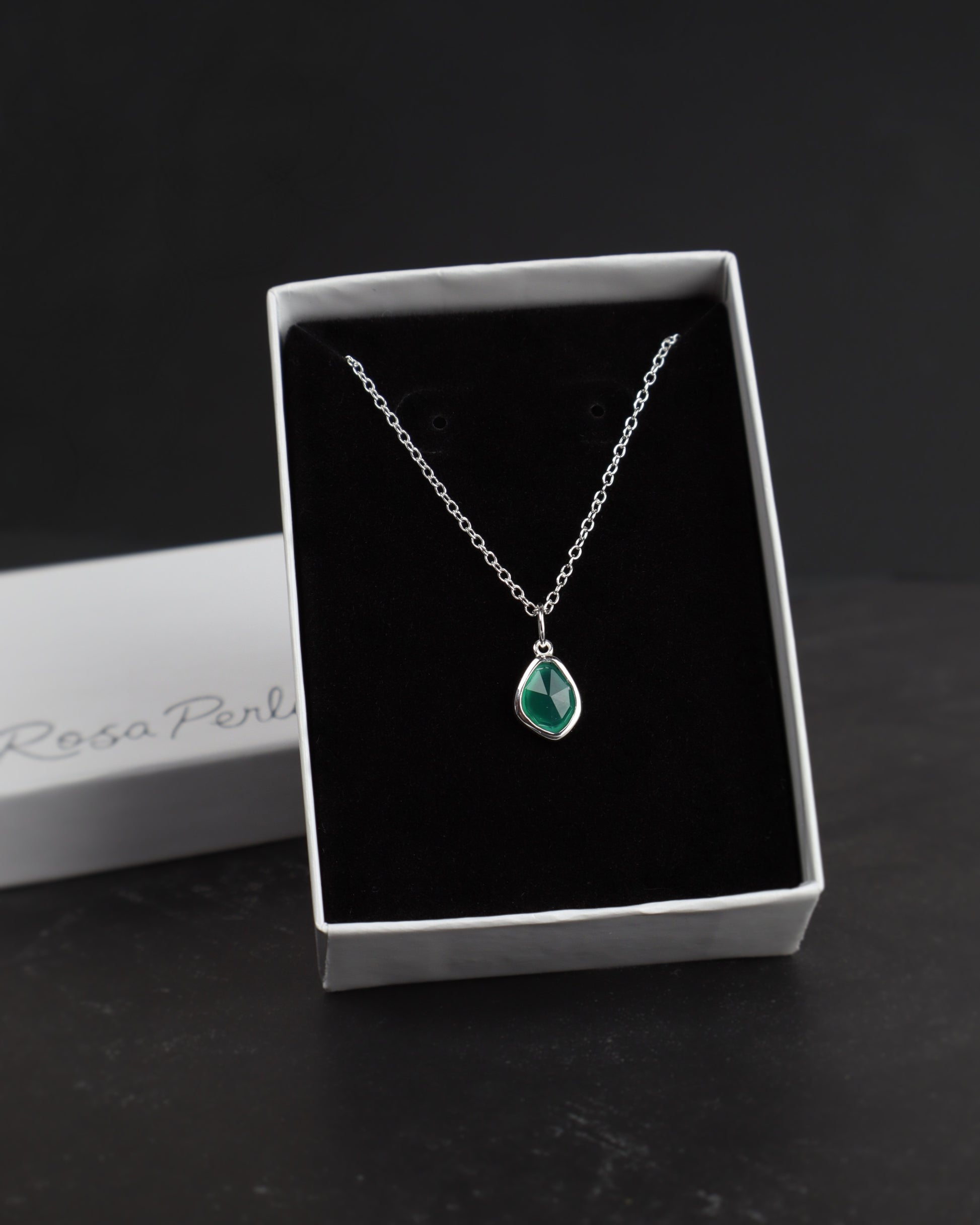 Silver necklace with a green pendant in a white box on a dark surface