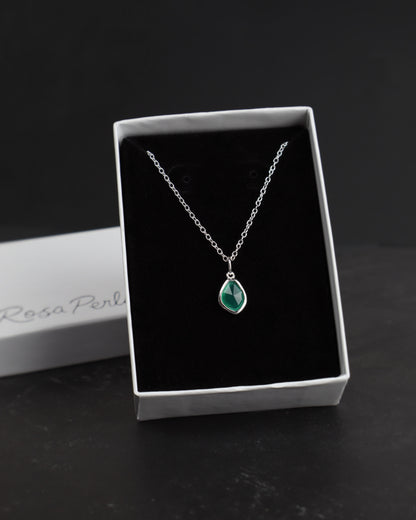 Silver necklace with a green pendant in a white box on a dark surface