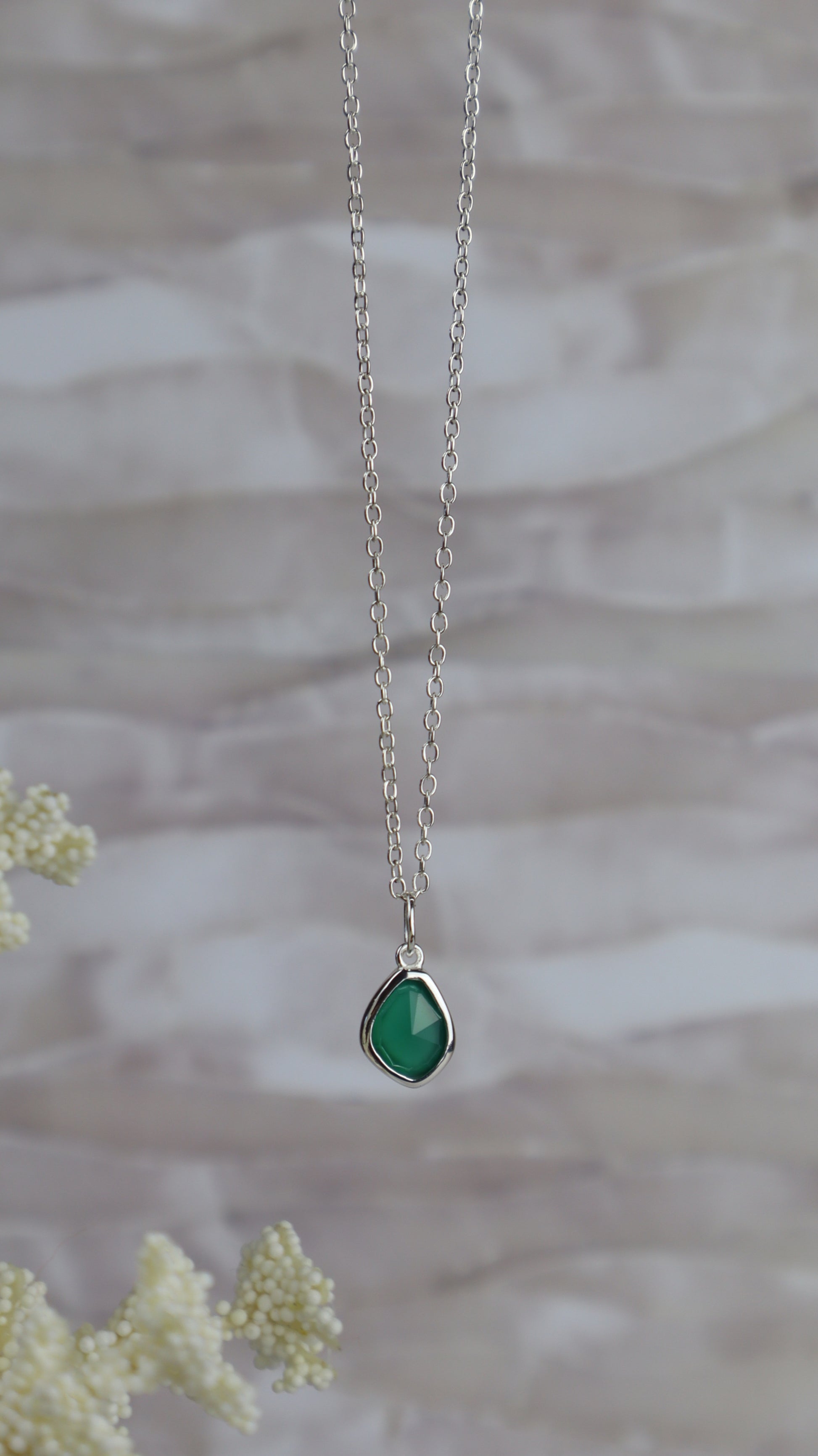 Necklace with a green teardrop pendant on a blurred natural background
