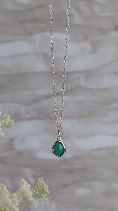 Necklace with a green teardrop pendant on a blurred natural background