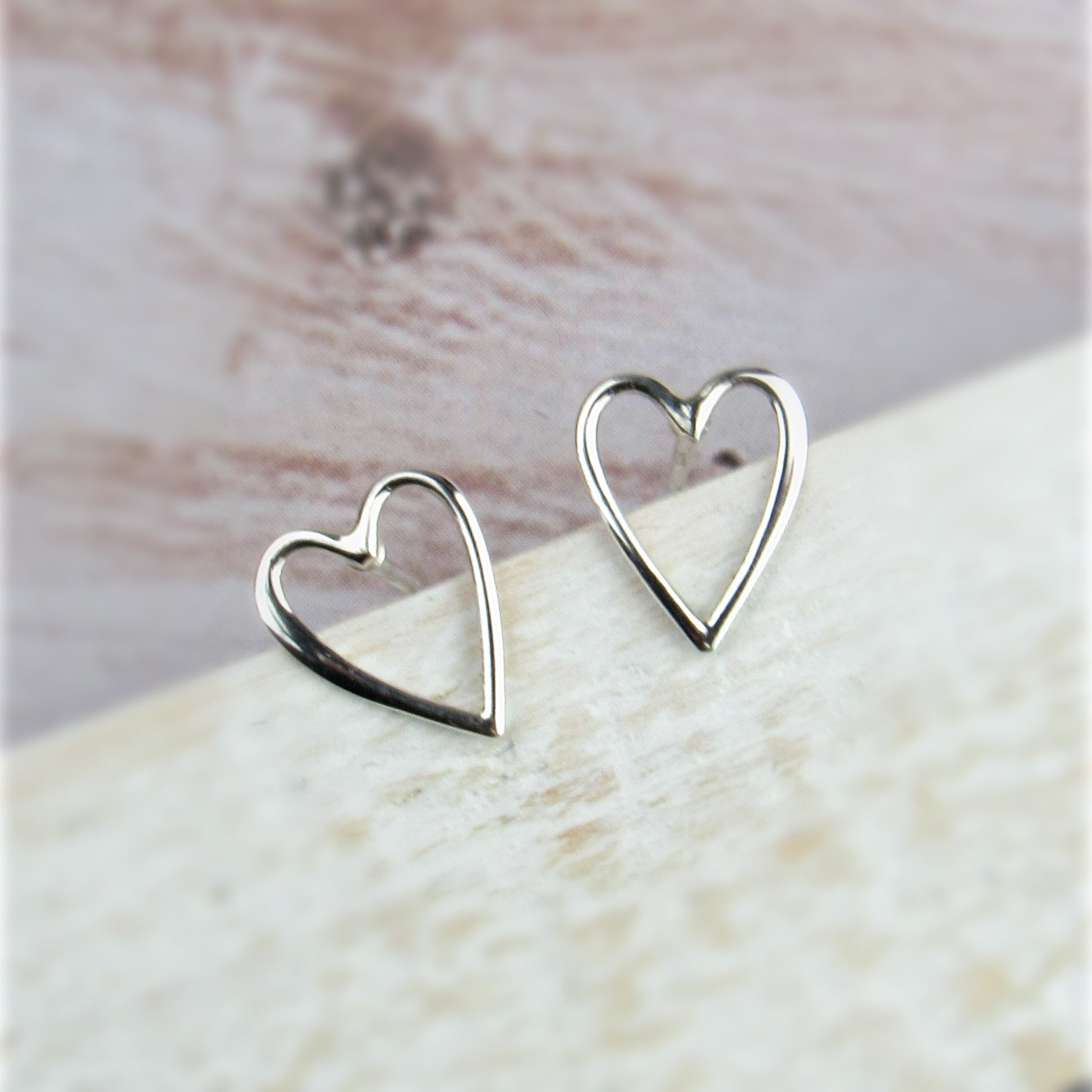 Silver heart-shaped earrings on a light wooden surface