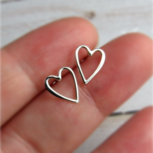Silver heart-shaped earrings held between fingers 