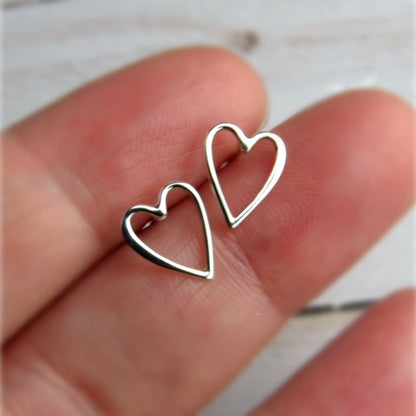 Silver heart-shaped earrings held between fingers 