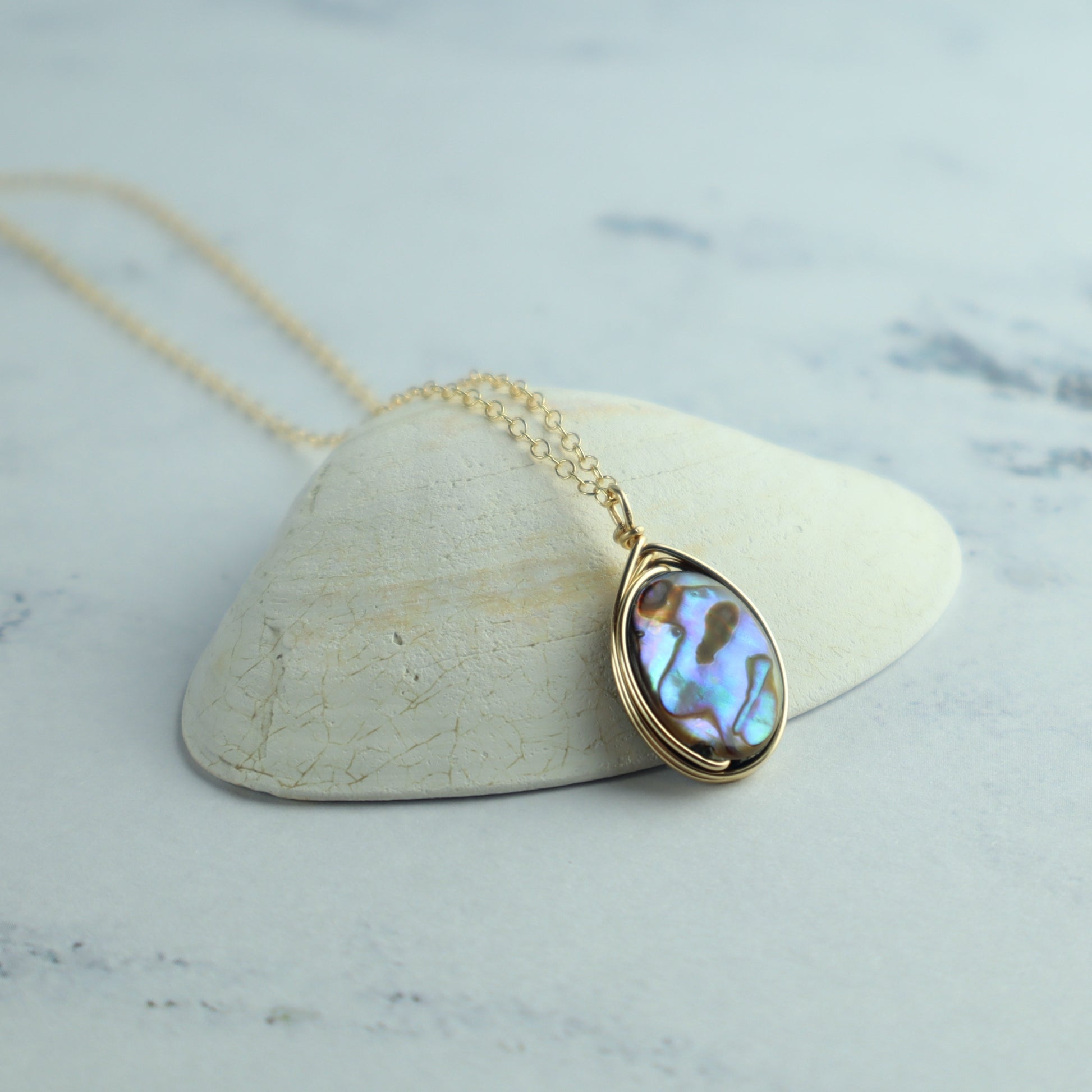 Gold necklace with a abalone pendant on a marble surface
