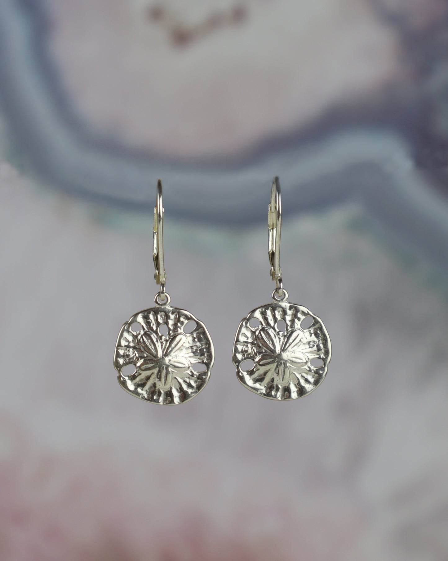 Silver sand dollar earrings on a blurred background