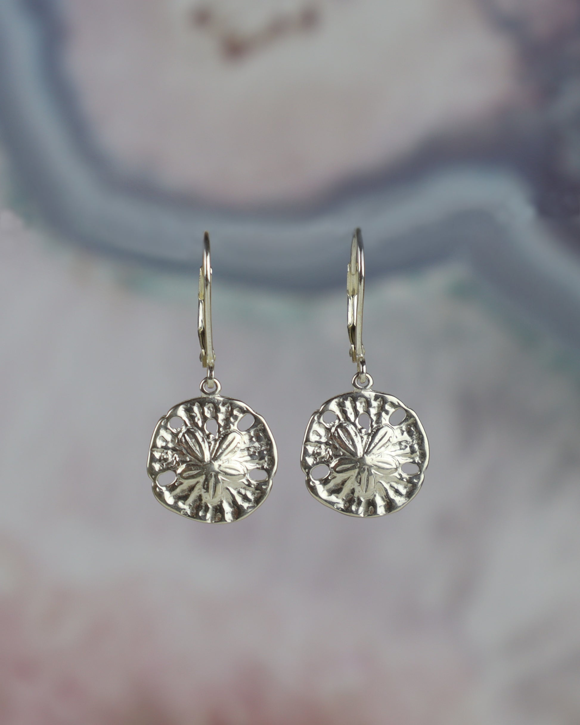 Silver sand dollar earrings on a blurred background