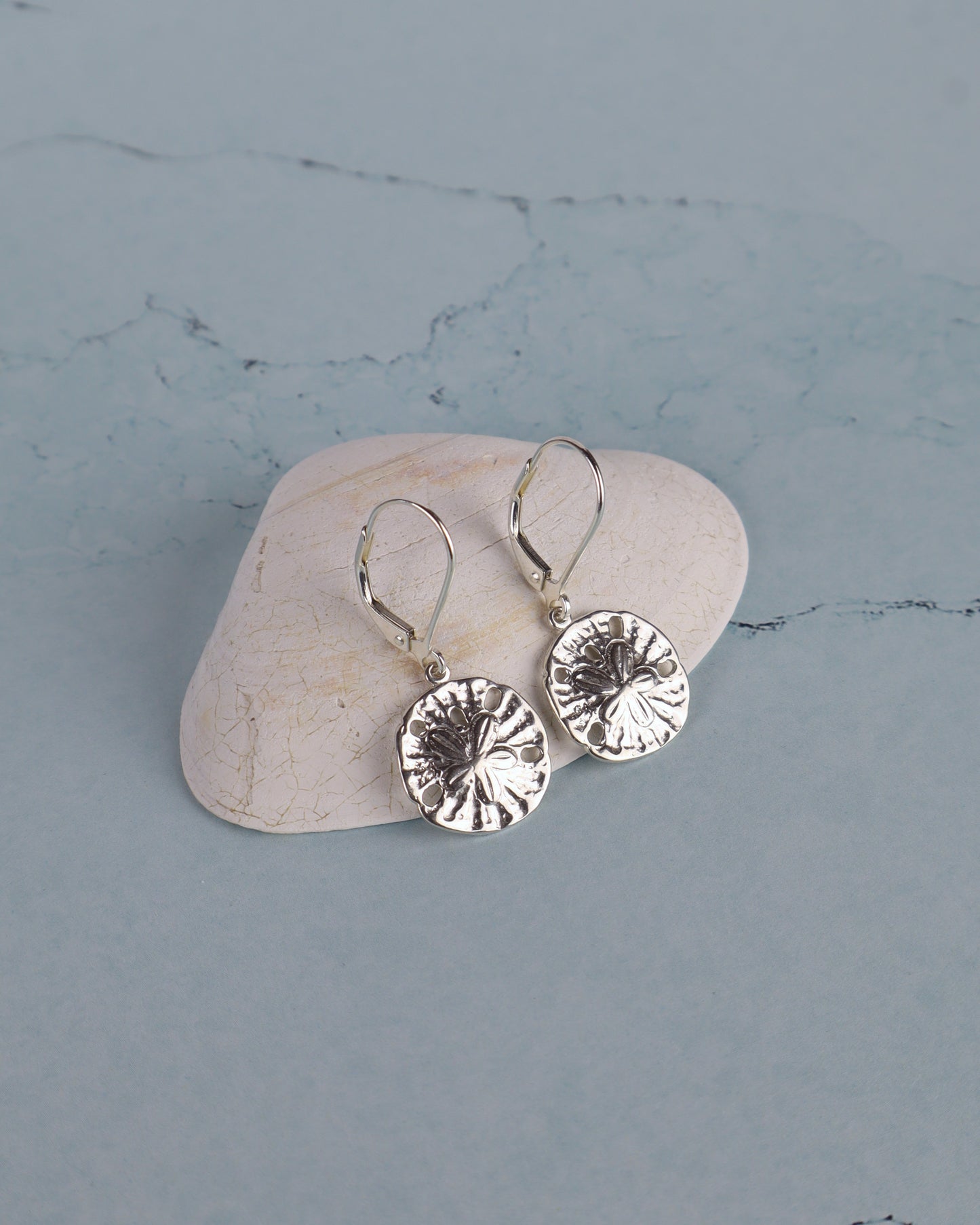sterling sand dollar earrings resting on a shell