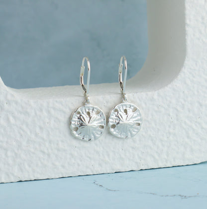 Silver sand dollar earrings on a textured white surface with a blue background